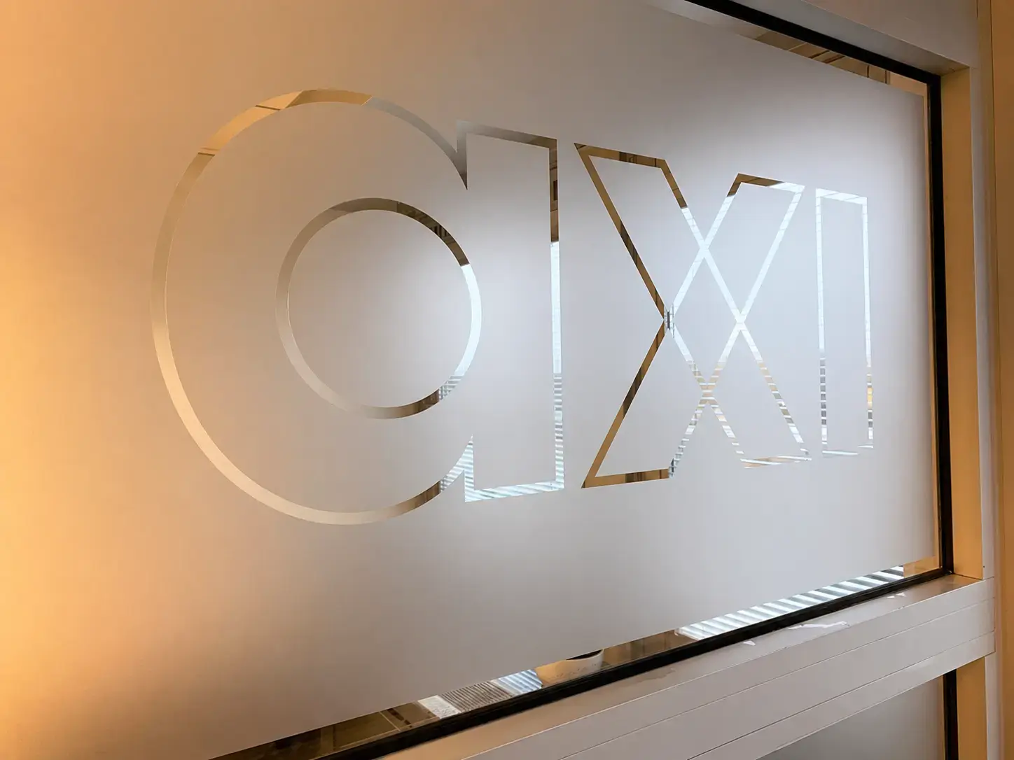 Glazen binnenwand met matte privacyfolie en uitgespaard axi-logo als interieurbelettering in een modern kantoor.