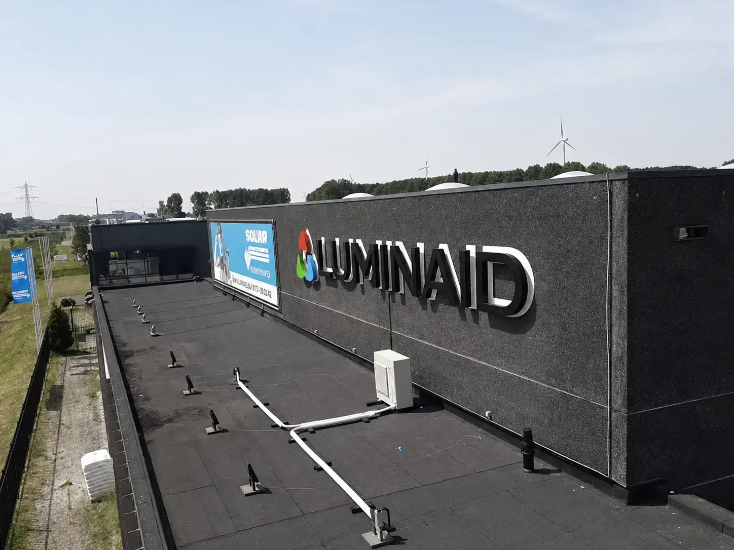 Donkere gevel van een bedrijfspand met gevelreclame van Luminaid, bestaande uit een full-colour logo en witte 3D doosletters langs een plat dak.