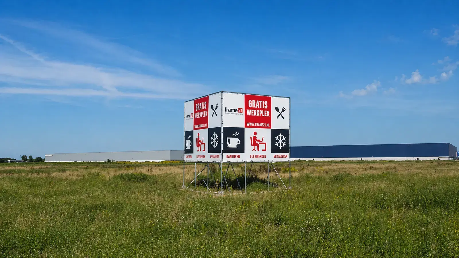Groot vrijstaand bouwbord met frame21, GRATIS WERKPLEK en pictogrammen voor kantoren, flexwerken en vergaderen op een metalen frame in een grasveld.