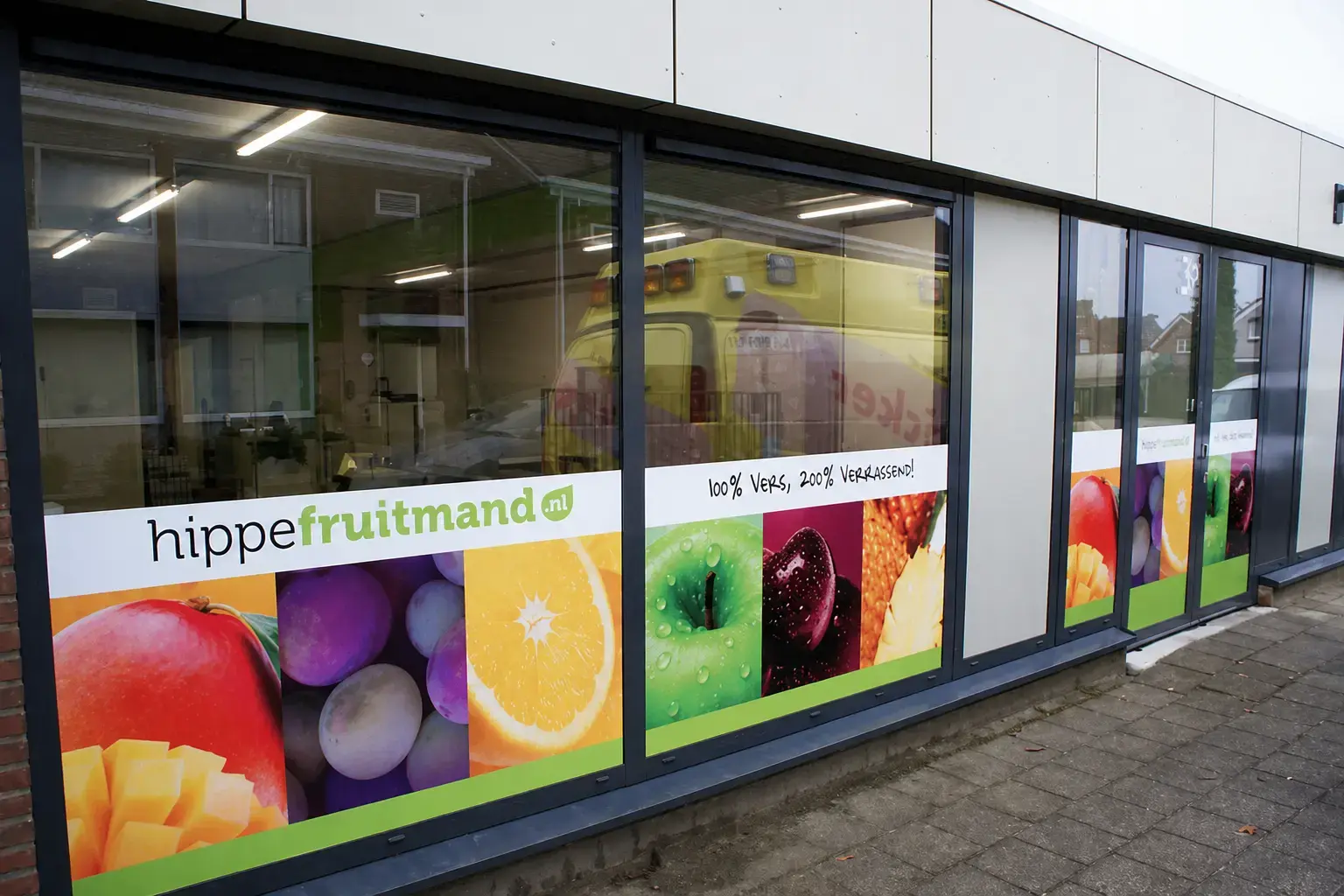 Raamstickers met kleurrijke fruitafbeeldingen en hippefruitmand.nl belettering op de glazen gevel van een winkelpand.