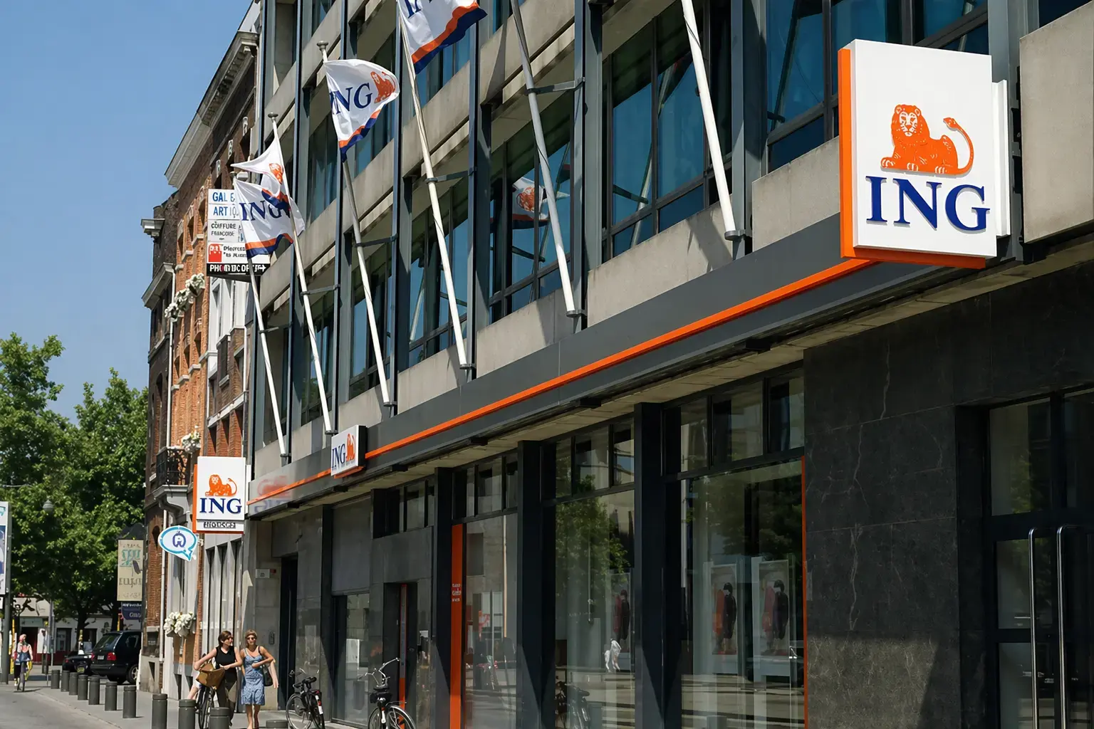 Moderne bankgevel met verlichte ING-uithangborden, gevelbelettering en mastvlaggen aan een glazen kantoorpand in de binnenstad.