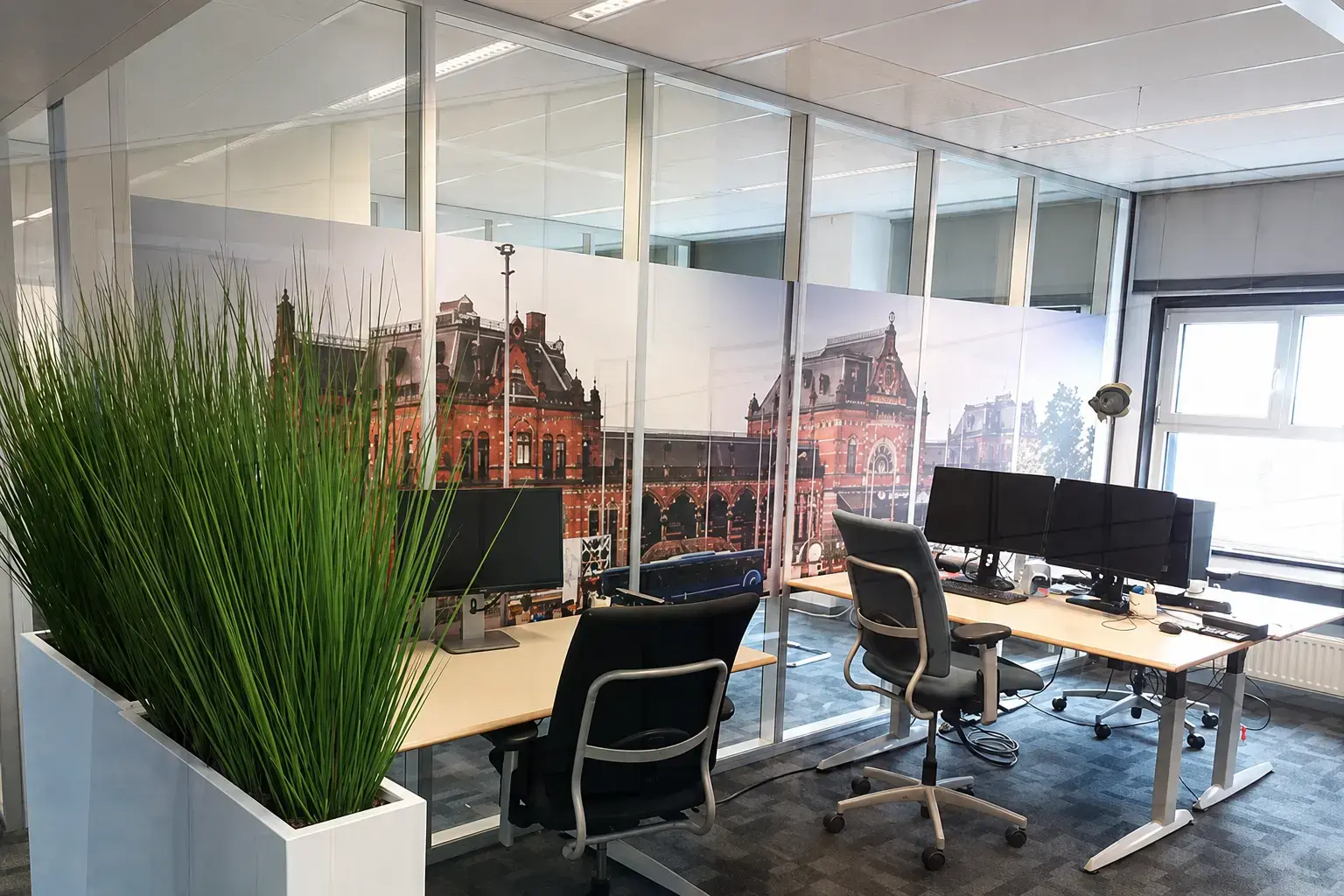 Glazen kantoorwand met privacyfolie en grootformaat fotoprint van een historisch gebouw als decoratieve raamfolie in een moderne werkruimte.