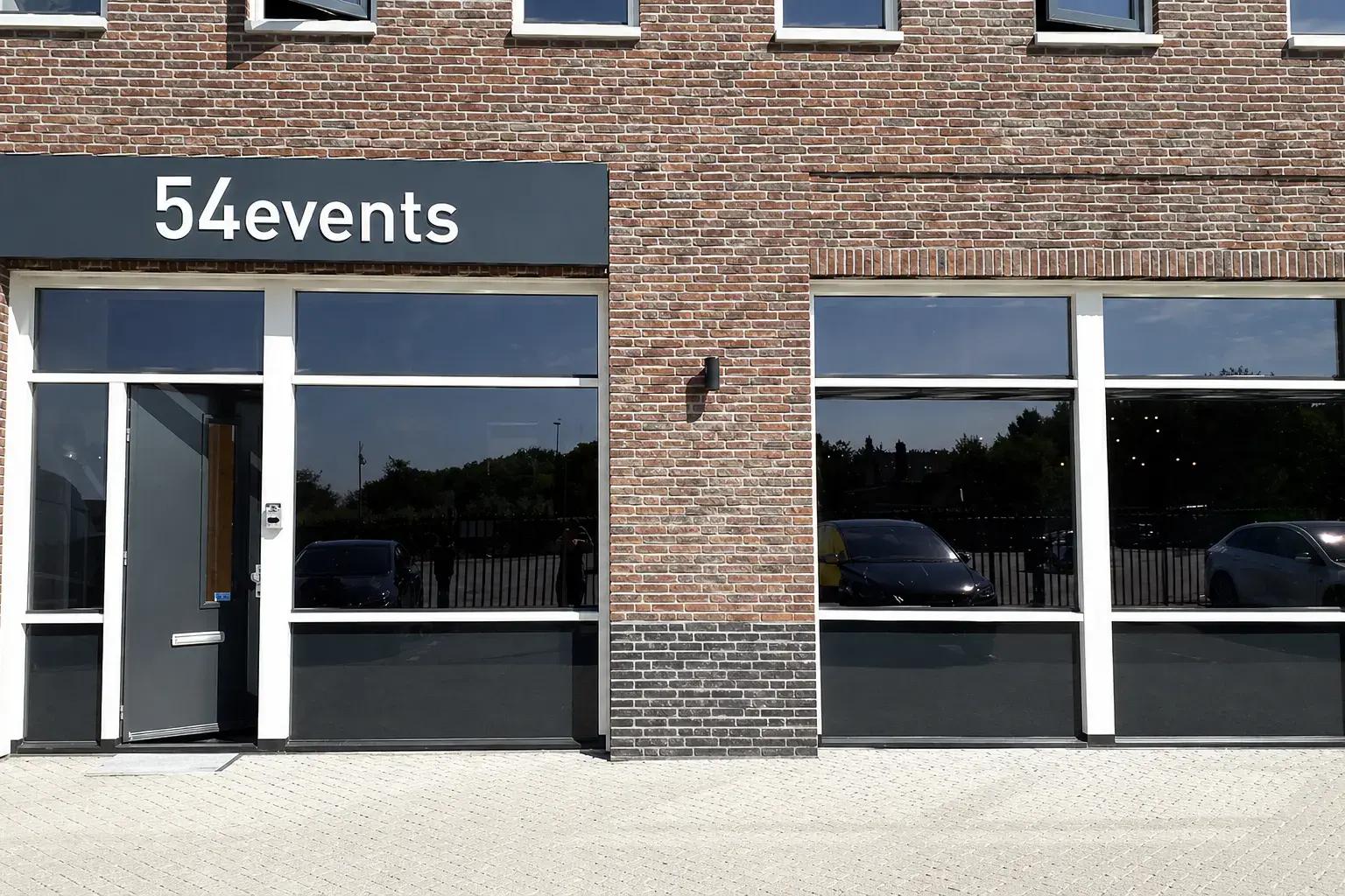 Gevelreclame met witte 54events letters op een donker gevelbord boven de entree van een bakstenen bedrijfspand.
