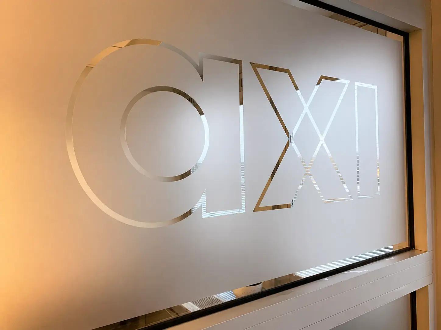 Glazen binnenwand met matte privacyfolie en uitgespaard axi-logo als interieurbelettering in een modern kantoor.