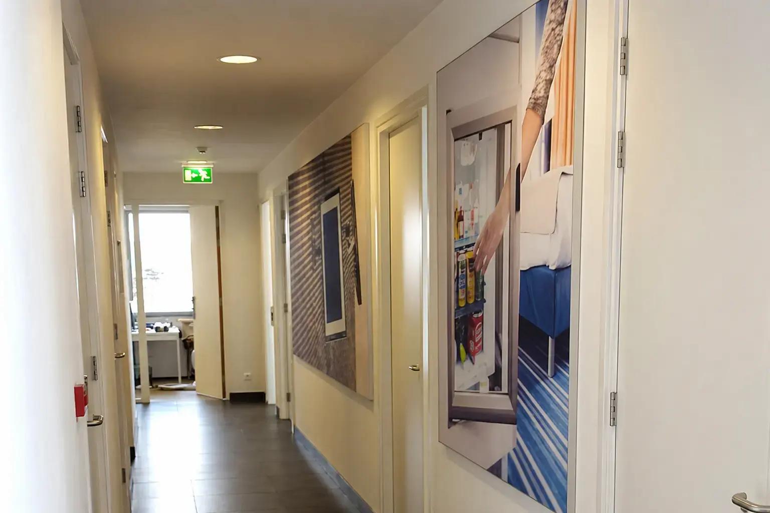 Gang met grote fotoprint-wandpanelen op binnenmuren en verlichte nooduitgangsigning, toegepast als decoratieve interieurbelettering en wayfinding.