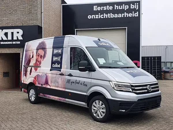 Grijze bestelbus met full-colour voertuigbelettering en reclamewrap voor diervoeding, voorzien van grote fotoprint en geparkeerd voor een bedrijfspand.