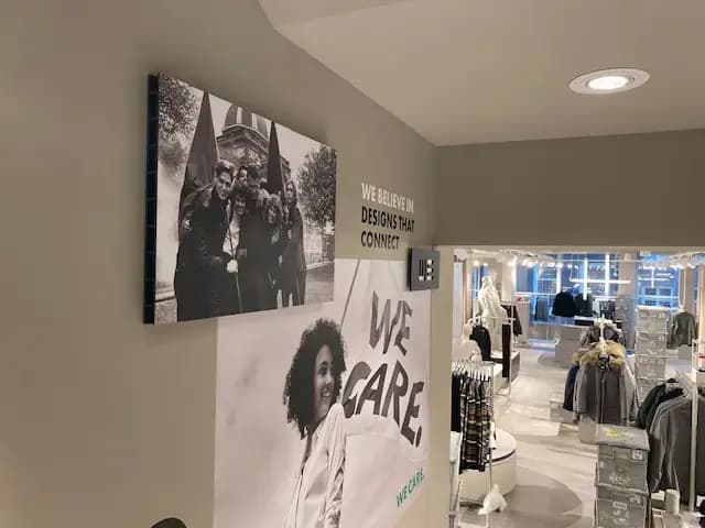 Winkelinterieur met wandvisuals en interieurbelettering met de teksten "WE CARE" en "WE BELIEVE IN DESIGNS THAT CONNECT" naast een doorgang naar de kledingwinkel.