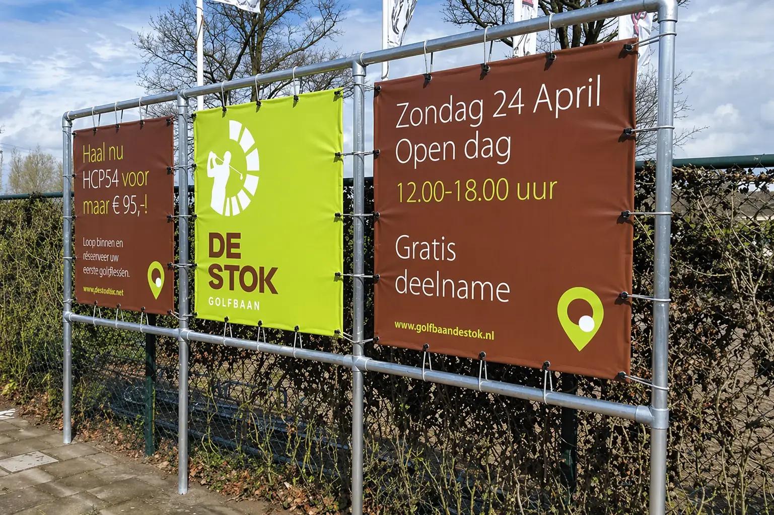 Drie outdoor spandoeken in een metalen buizenframe voor De Stok Golfbaan met promotie voor een open dag en golflessen.