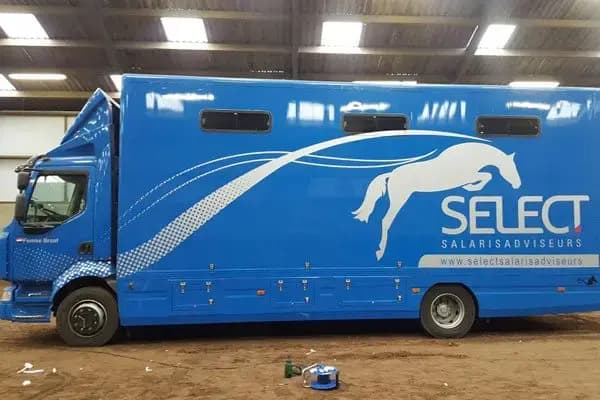 Blauwe paardenvrachtwagen met grote witte paardenafbeelding, SELECT Salarisadviseurs-belettering en website op de zijkant, gefotografeerd in een werkplaats.
