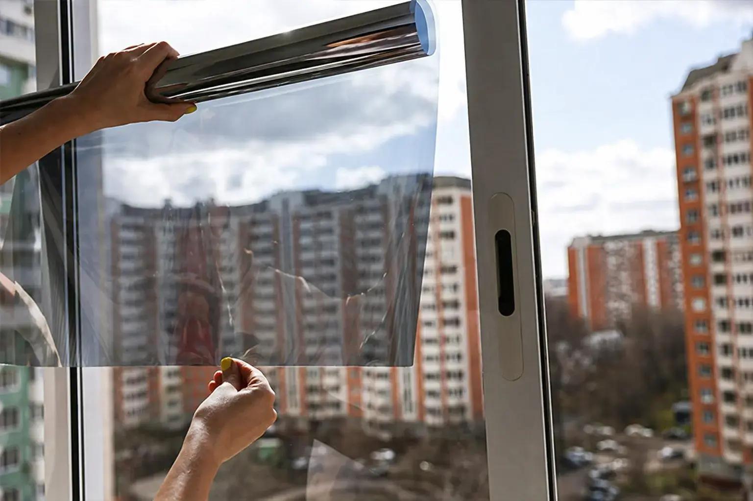 Transparante raamfolie wordt aangebracht op een raam voor zonwering en glasbescherming in een stedelijke omgeving.