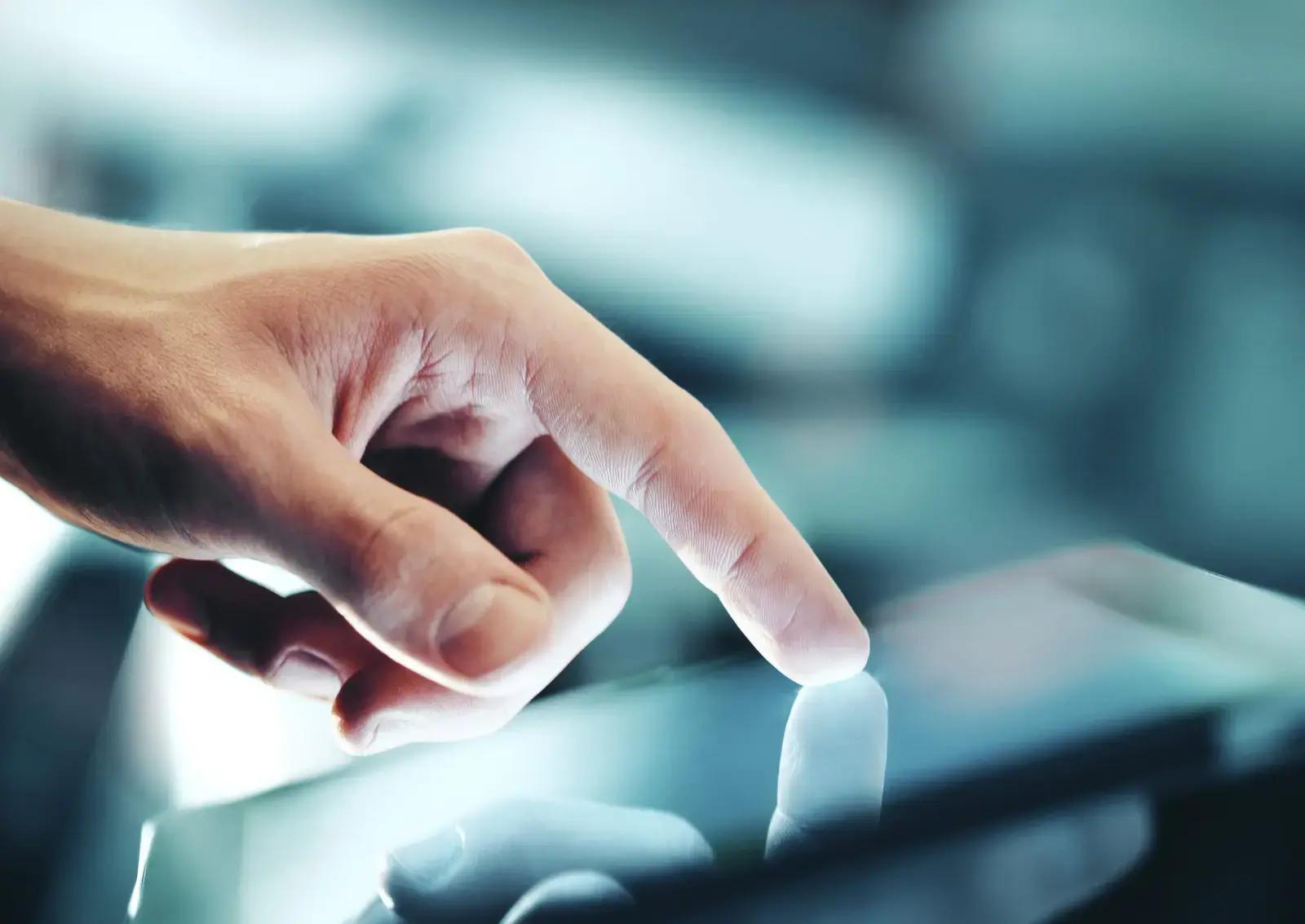 Hand die een verlicht touchscreen aanraakt, met reflectie op het glas en onscherpe digitale omgeving op de achtergrond.