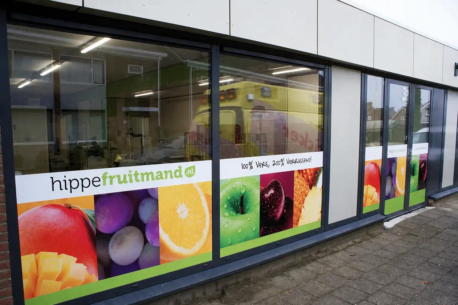Raamstickers met kleurrijke fruitafbeeldingen en hippefruitmand.nl belettering op de glazen gevel van een winkelpand.