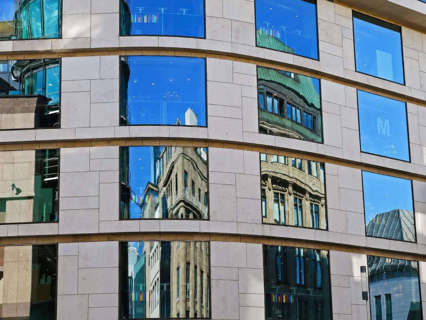 Moderne gevel met blauwe glasramen en subtiele kleurrijke raamfolie, waarin omliggende gebouwen weerspiegelen als opvallende architectonische glasvisual.