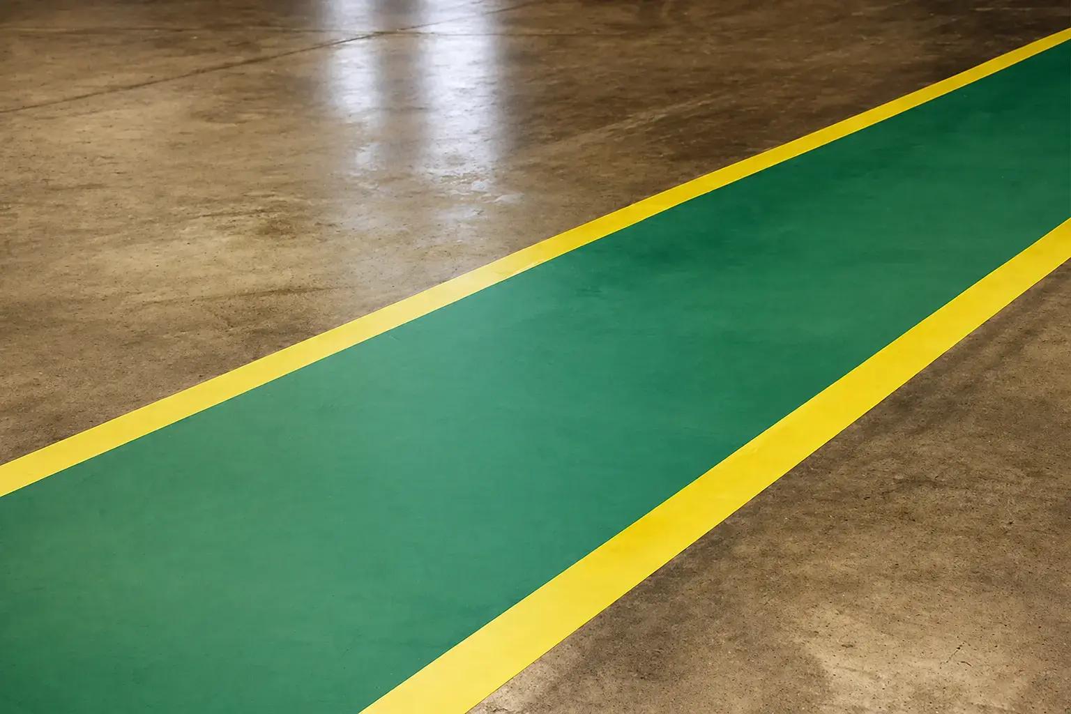 Groene looproute met gele vloerbelijning op een industriële betonvloer, toegepast als duidelijke veiligheidsmarkering in een magazijnomgeving.