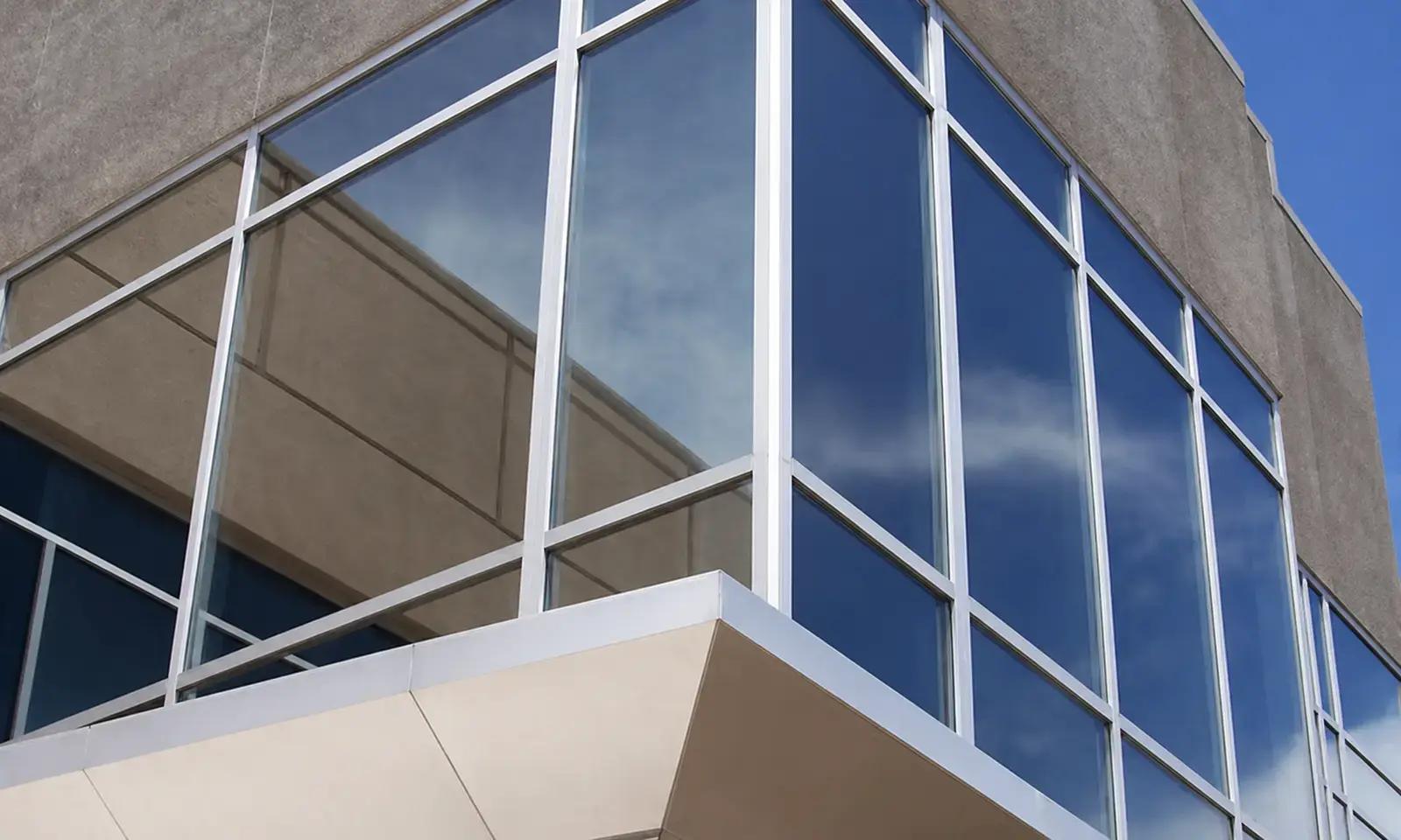 Reflecterende blauwe raamfolie op grote glaspartijen van een kantoorgevel met aluminium kozijnen.