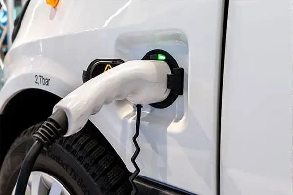 Close-up van een laadkabel in het laadpunt van een witte elektrische bedrijfswagen, met groene laadindicator en detail van de voertuigzijde.