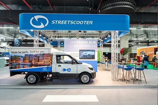 Beursstand van StreetScooter met ronde hangende lichtbak, elektrische bestelwagen met full-color voertuigbelettering en promotionele achterpanelen in een indoor evenementenhal.