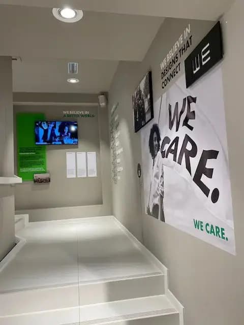 Gang met grote wandvisuals, interieurbelettering en digitale display met de slogans "WE CARE" en "WE BELIEVE IN DESIGNS THAT CONNECT" in een modern winkelinterieur.