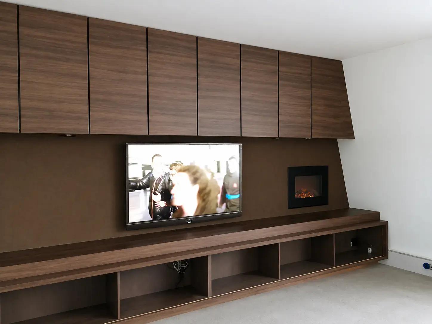 Maatwerk interieurwand met houten wandpanelen, ingebouwde tv en elektrische haard, toegepast als strakke decoratieve wandbekleding in een woonruimte.