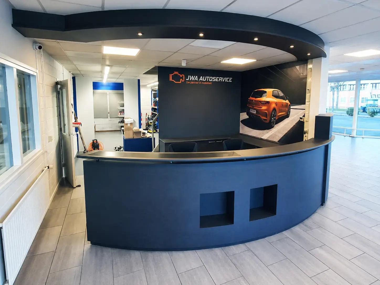 Autogarage receptie met JWA Autoservice wandlogo, fotoprint van een oranje auto en donkere balie als opvallende interieurreclame.