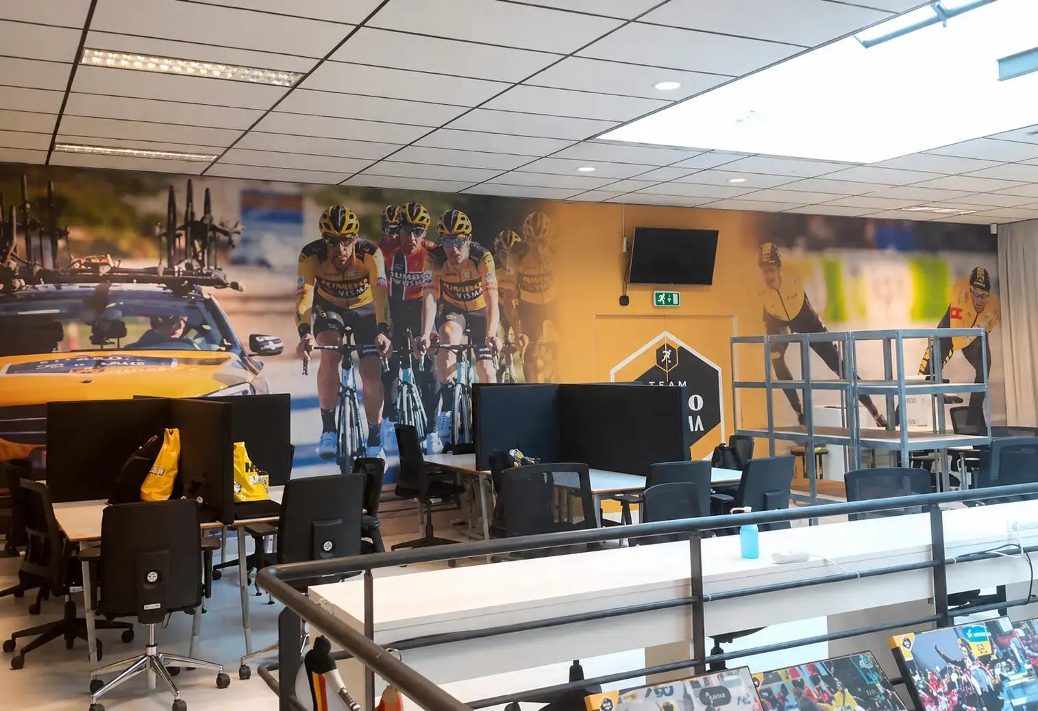 Kantoorruimte met kamerbrede wandprint van Team Jumbo-Visma wielrenners, toegepast als opvallende interieurvisual en decoratieve wandbekleding achter werkplekken.