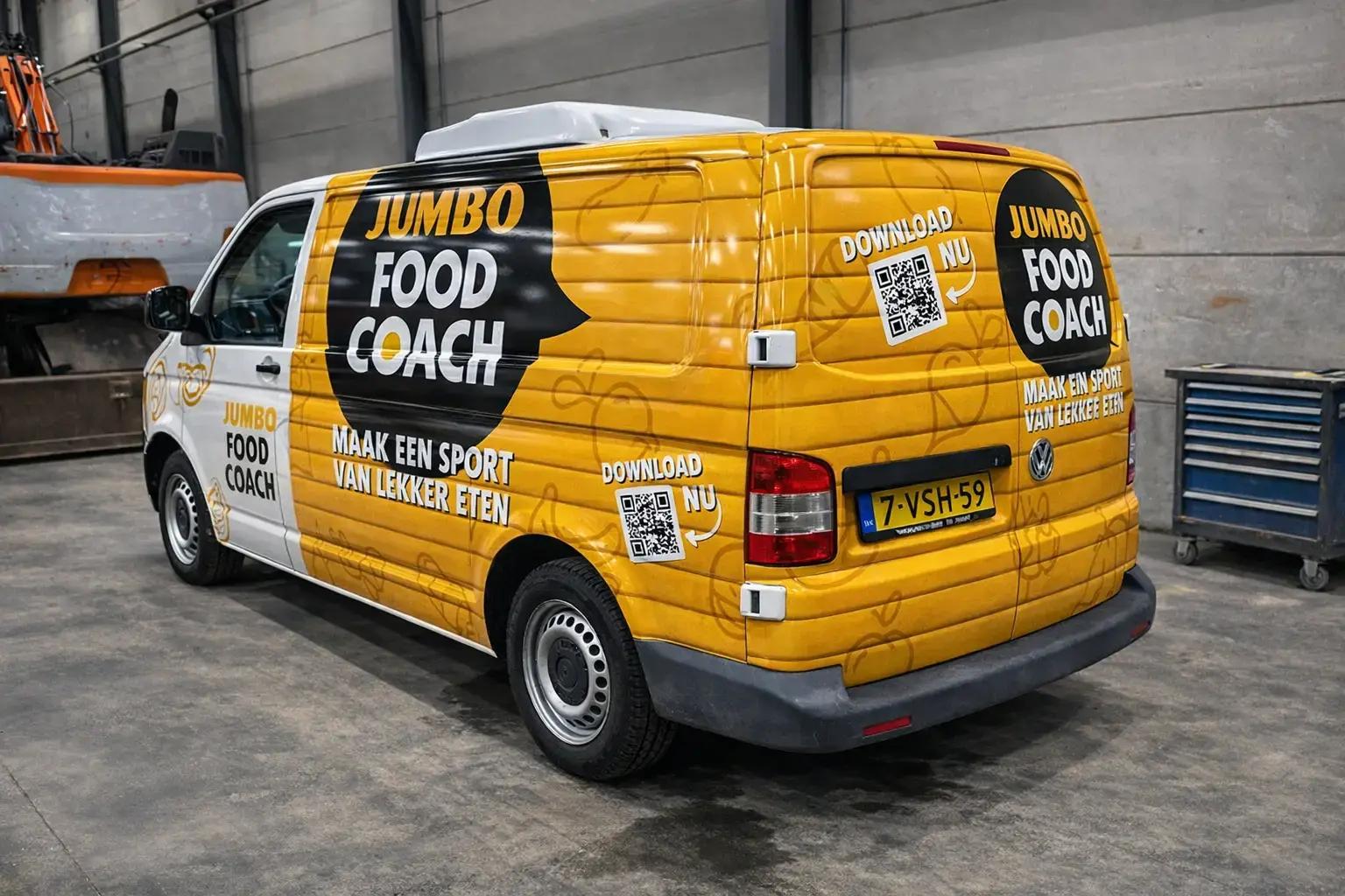 Gele en witte bestelbus met full wrap voertuigbelettering van Jumbo Food Coach, voorzien van grote reclameteksten, QR-codes en promotionele autobelettering in een werkplaats.