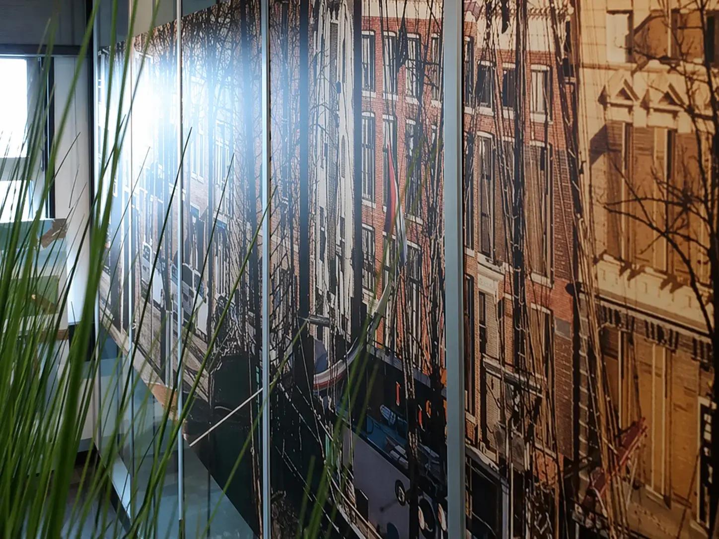 Glazen kantoorwand met full-colour glasfolie van Amsterdamse gevels en grachtenpanden, toegepast als decoratieve privacyfolie in een moderne werkomgeving.