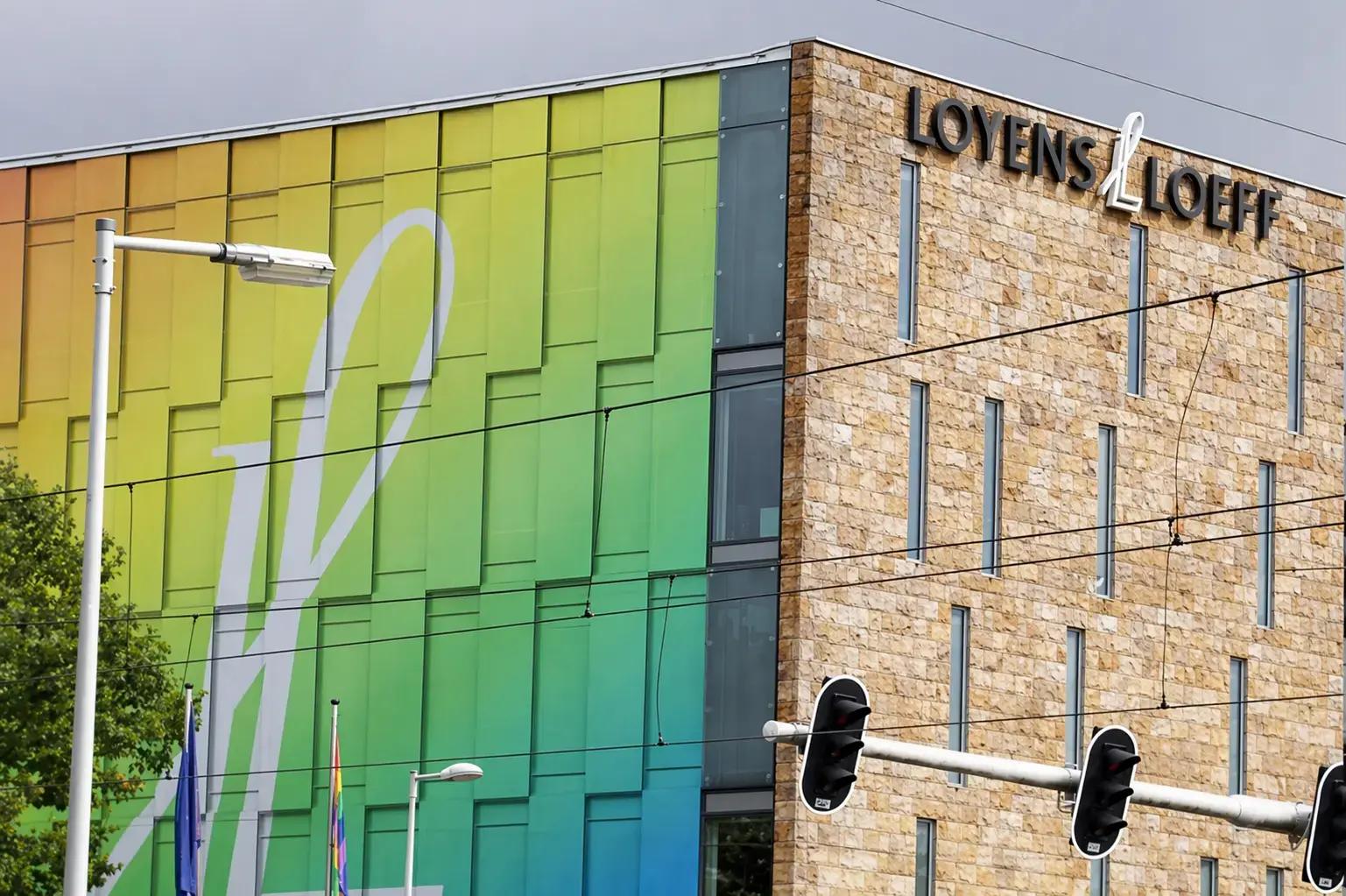 Gevelreclame met 3D letters Loyens & Loeff op een natuurstenen gebouw naast een kleurrijke gevelwand met groot wit beeldmerk.