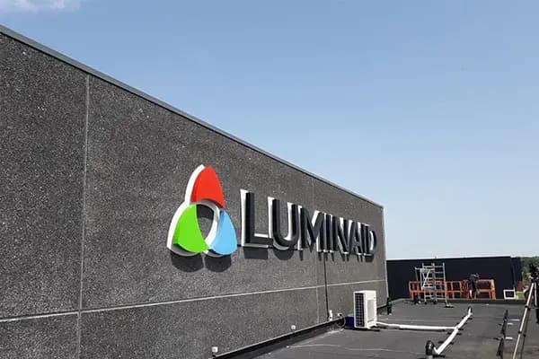 Donkere gevel van een bedrijfspand met gevelreclame van Luminad, bestaande uit een full-colour logo en zwarte 3D doosletters op een plat dak.