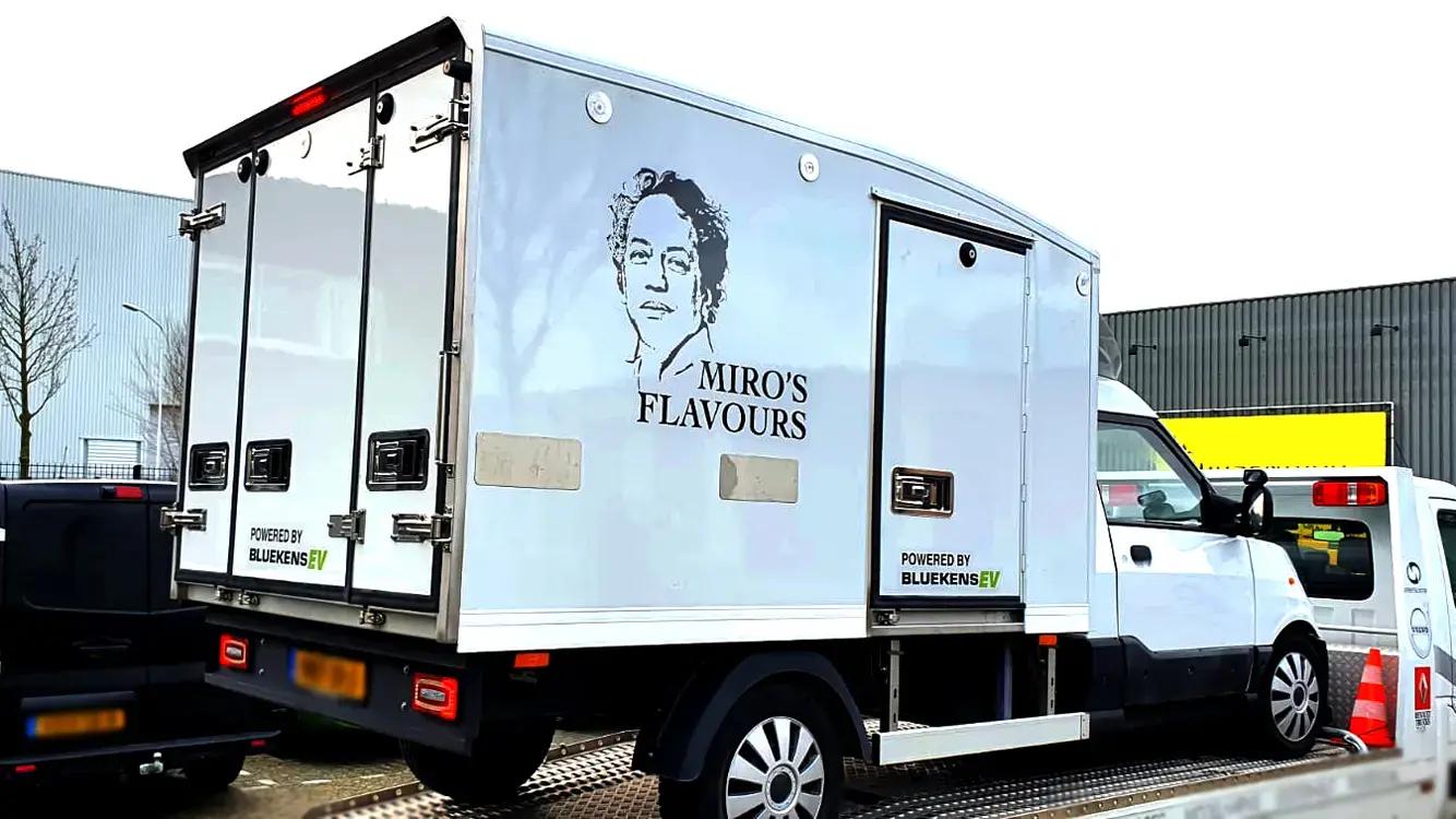 Witte bakwagen met voertuigbelettering voor Miro’s Flavours, voorzien van zwarte merknaam, portretillustratie en sponsorvermelding op de zij- en achterzijde van de laadbak.