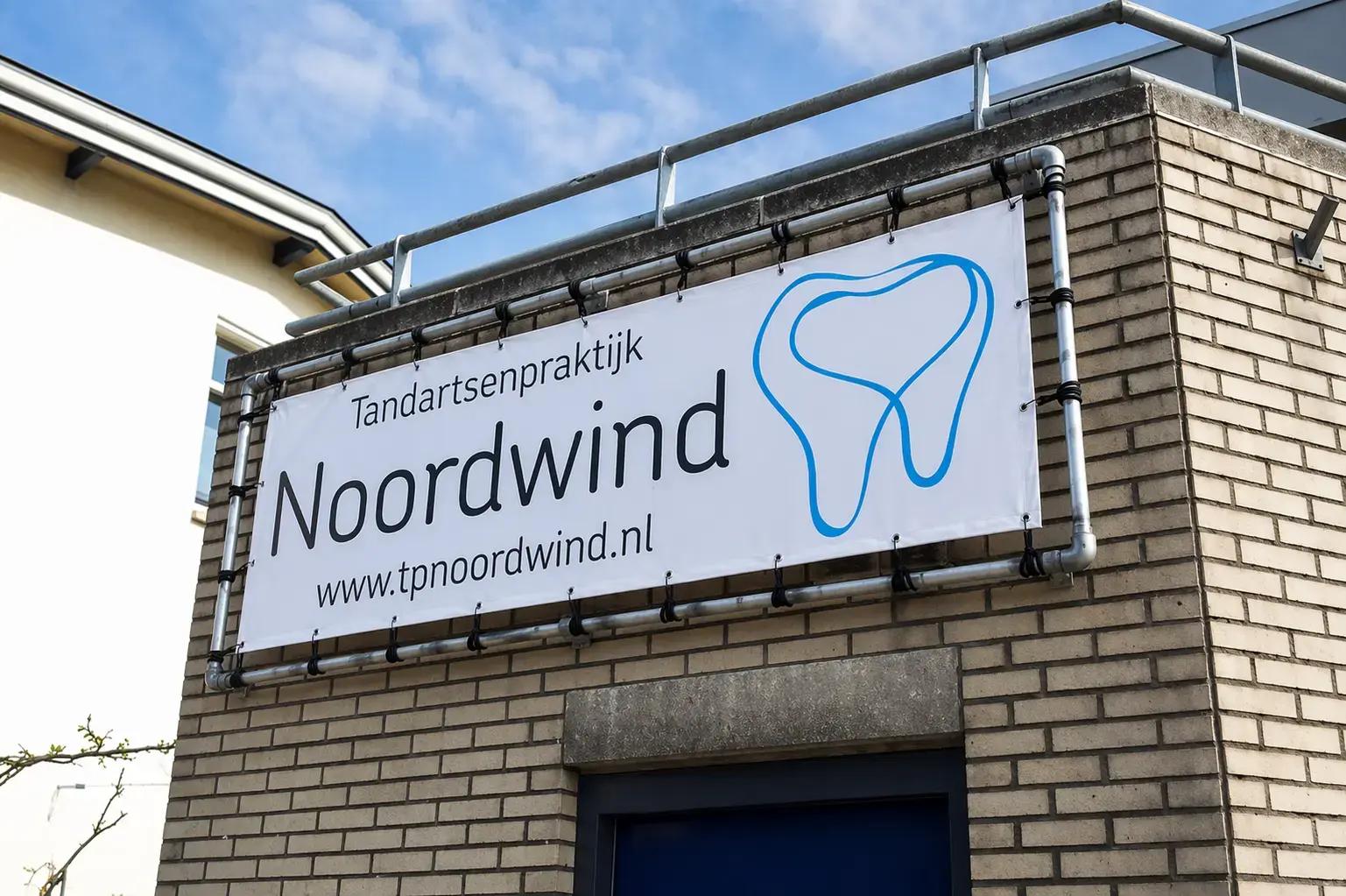 Witte gevelbanner in buizenframe voor Tandartsenpraktijk Noordwind met tandlogo op een bakstenen gevel.