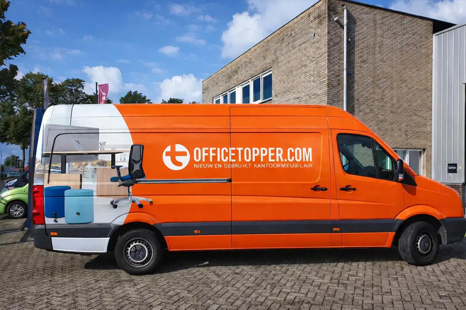 Oranje bestelbus met voertuigbelettering en full-color carwrap van Officetopper.com, voorzien van wit logo, grote bedrijfsnaam en foto van kantoormeubilair op de zijkant, geparkeerd voor een bedrijfspand.