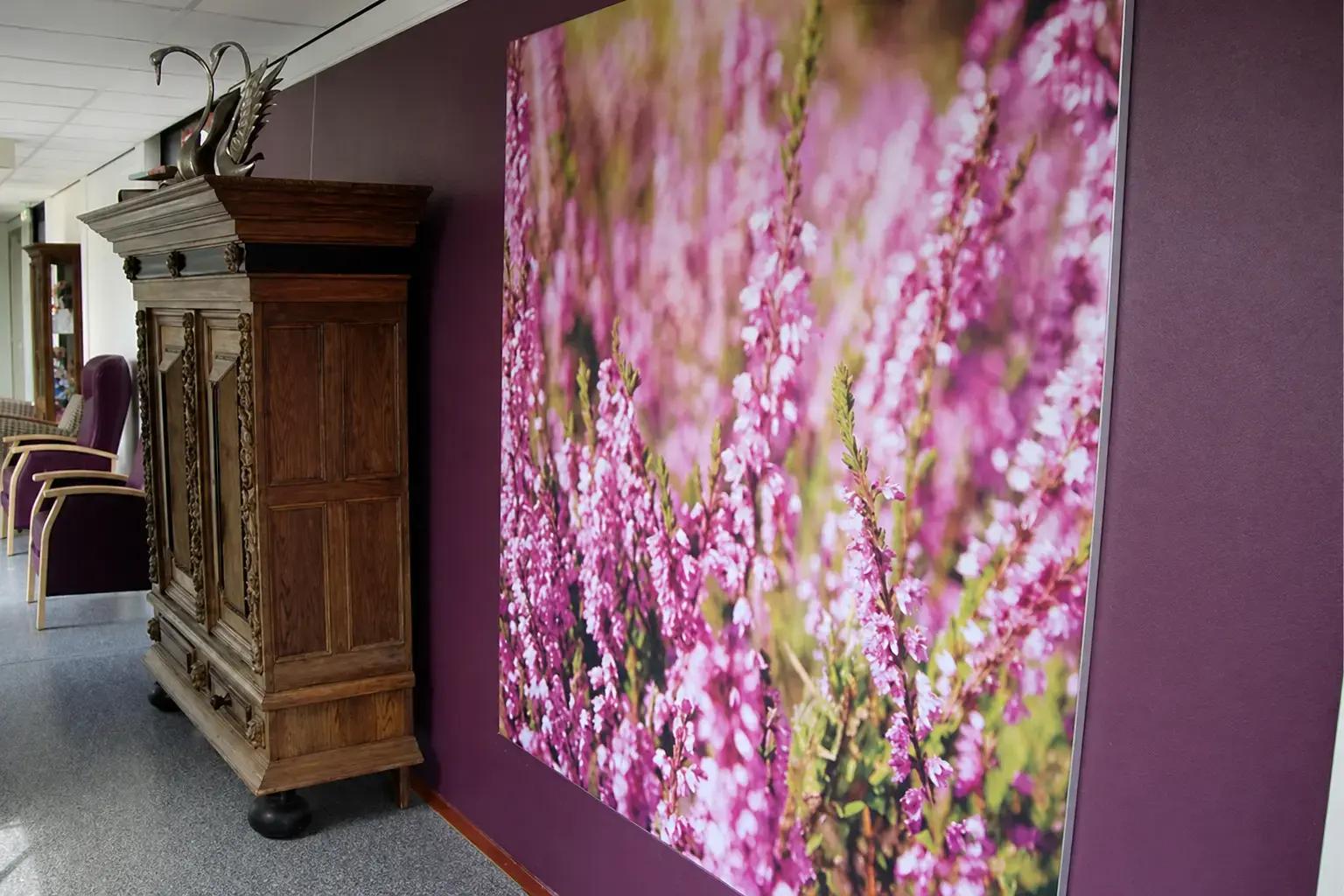 Grote wanddecoratie met fotoprint van paarse bloemen, strak gemonteerd op een paarse binnenmuur als sfeervolle interieurvisual.