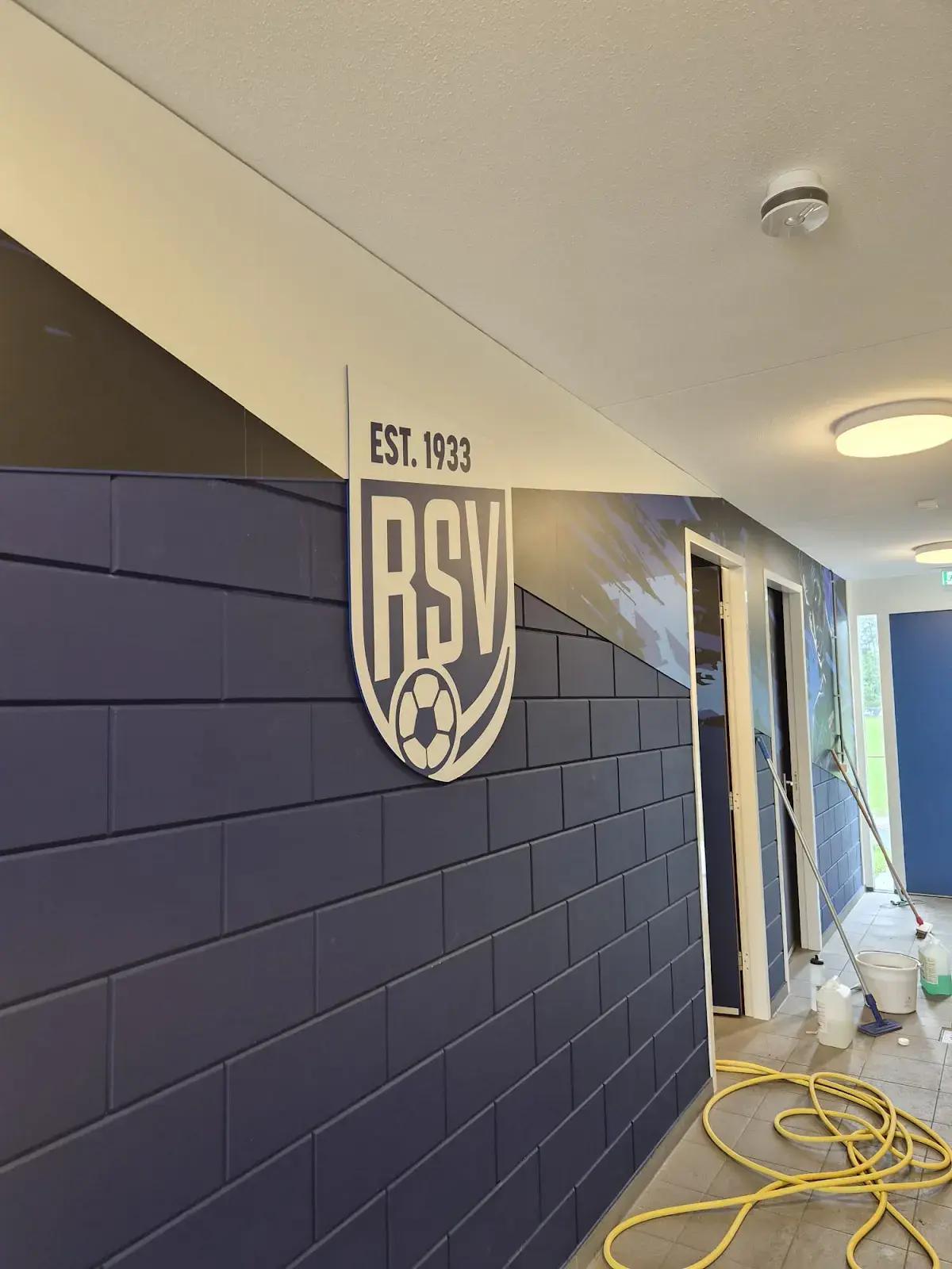 RSV-logo op de blauw-witte wand in de gang bij de kleedkamers.