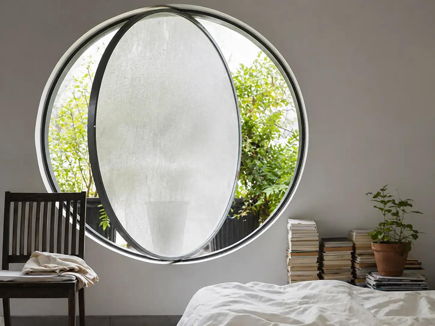 Rond raam met matte privacyfolie in een slaapkamer, met zwarte kozijnen en zicht op groen buiten.