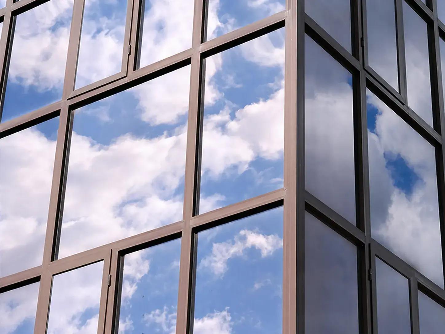 Glazen gevel met grote raamvlakken en reflectie van blauwe lucht met witte wolken, toegepast als opvallende architectonische glasafwerking.