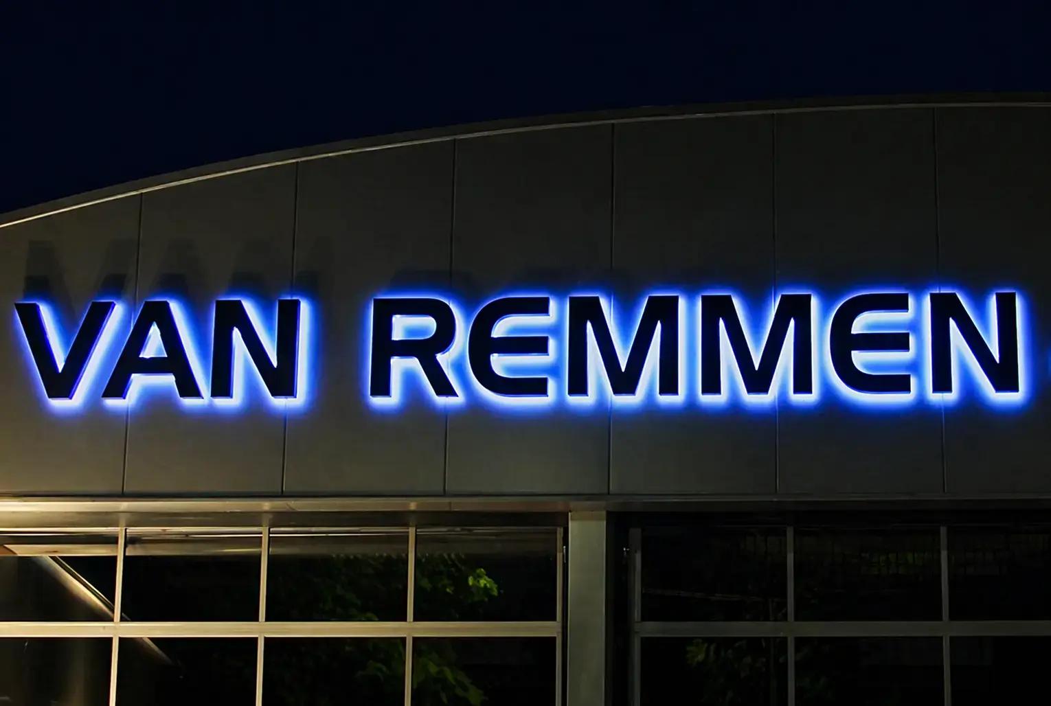 Blauwe halo-verlichte gevelletters met de tekst VAN REMMEN op een moderne bedrijfsgevel bij avond.