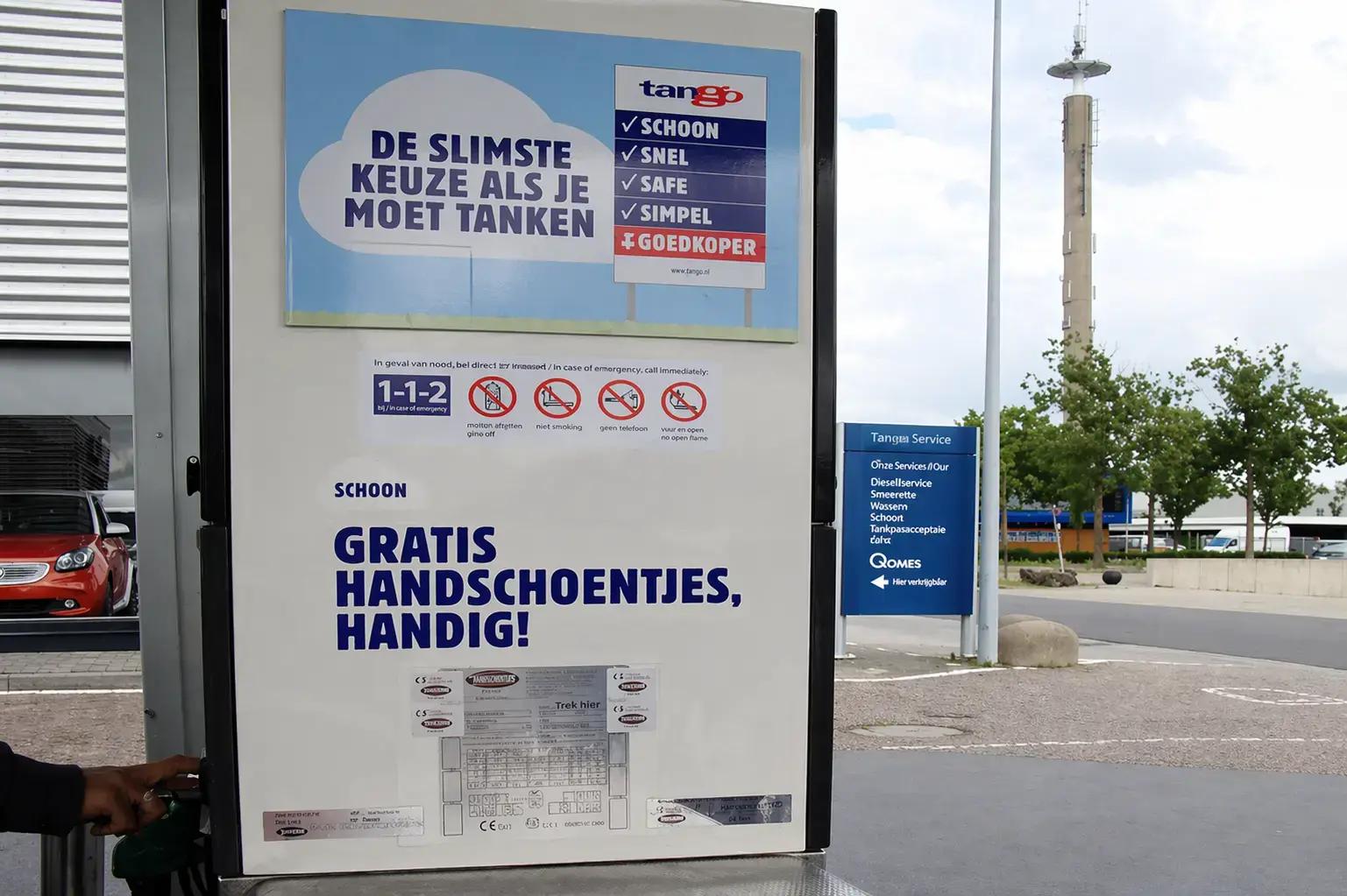 Informatieborden en veiligheidsstickers op een Tango-tankzuil, met promotiebord voor tanken en gratis handschoentjes bij een tankstation.