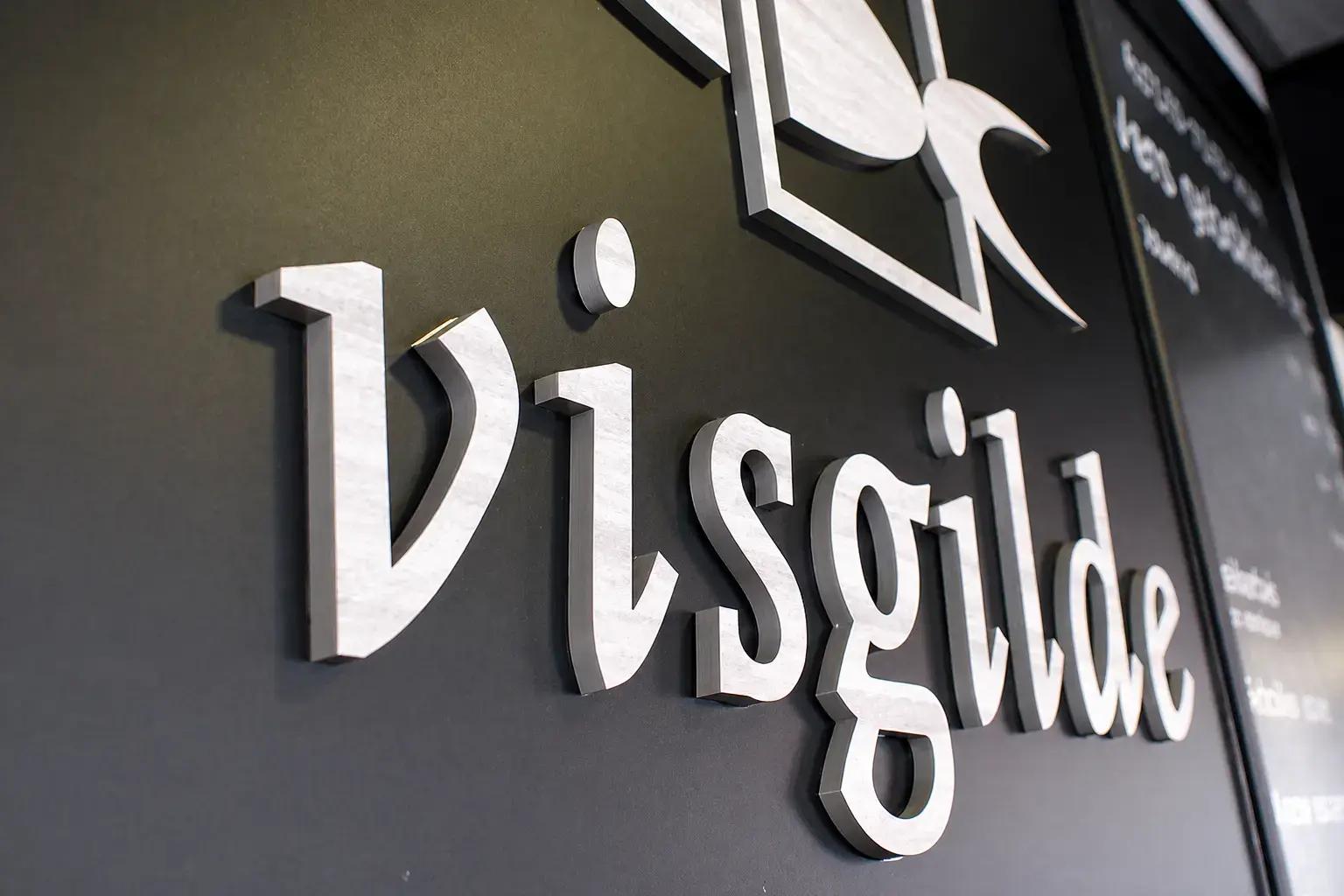 3D freesletters met Visgilde-logo op een donkere wand, uitgevoerd als opvallende binnenreclame met reliëf en metalen afwerking.