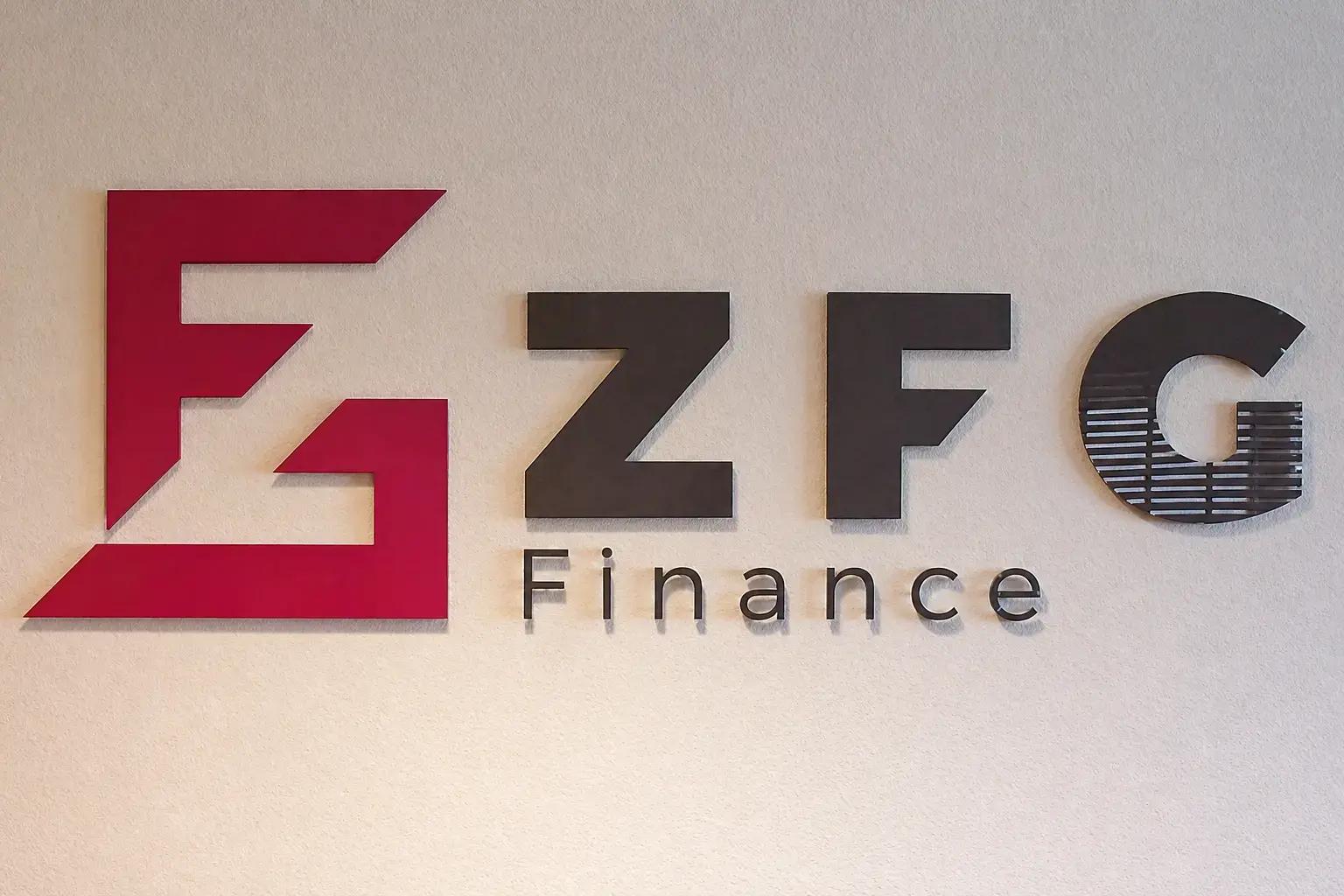 ZFG Finance wandlogo met rode beeldmerkplaat en zwarte 3D letters, gemonteerd op een lichte structuurmuur als zakelijke binnenreclame.