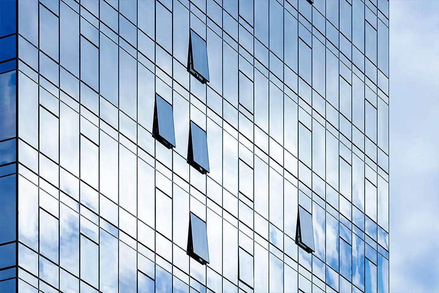 Glazen gevel met spiegelende raamvlakken en geopende kiepramen, waarin blauwe lucht en wolken reflecteren als strakke architectonische glasvisual.