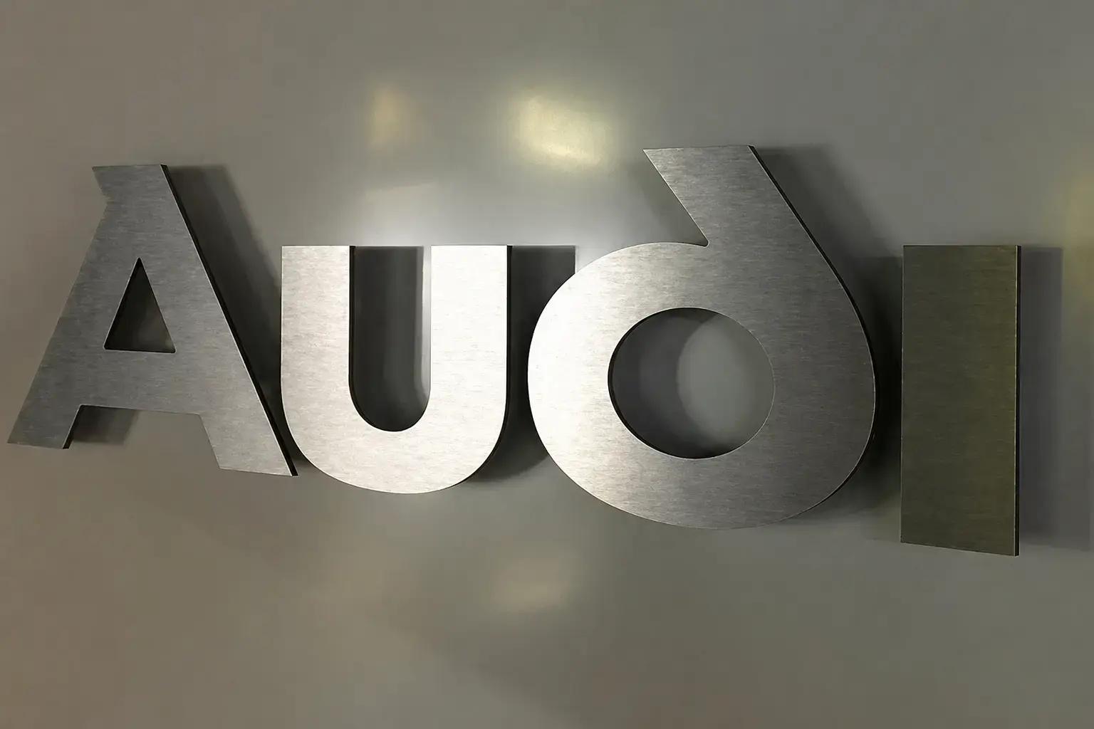 Metalen 3D wandletters met geborstelde afwerking, gemonteerd op afstandhouders tegen een grijze binnenmuur voor strakke bedrijfsreclame.