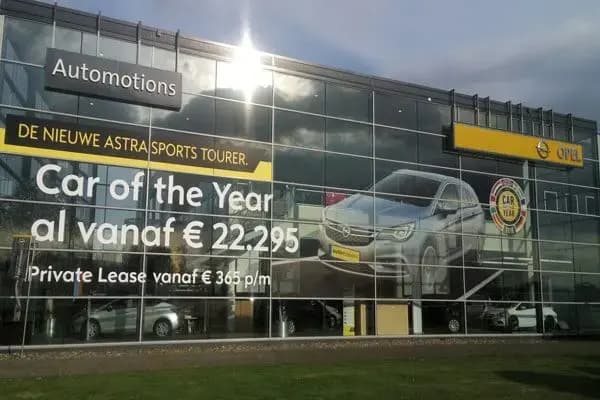 Glazen showroomgevel met full-color raambelettering voor Opel, inclusief groot beeld van een auto en promotionele actietekst voor de Astra Sports Tourer.