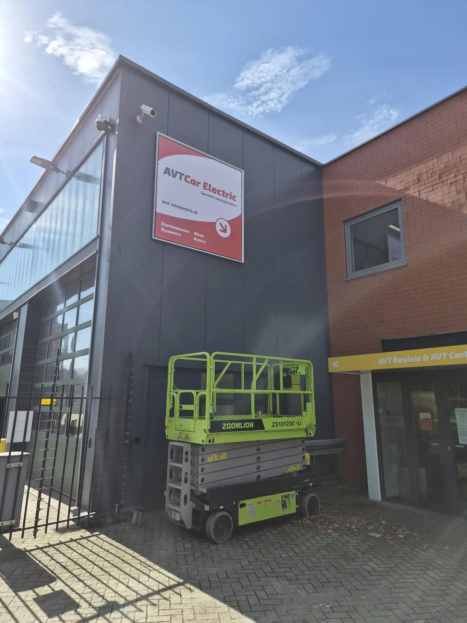 AVT Car Electric reclamedoek in een Triaflex frame, met hoogwerker voor de gevel tijdens montage.