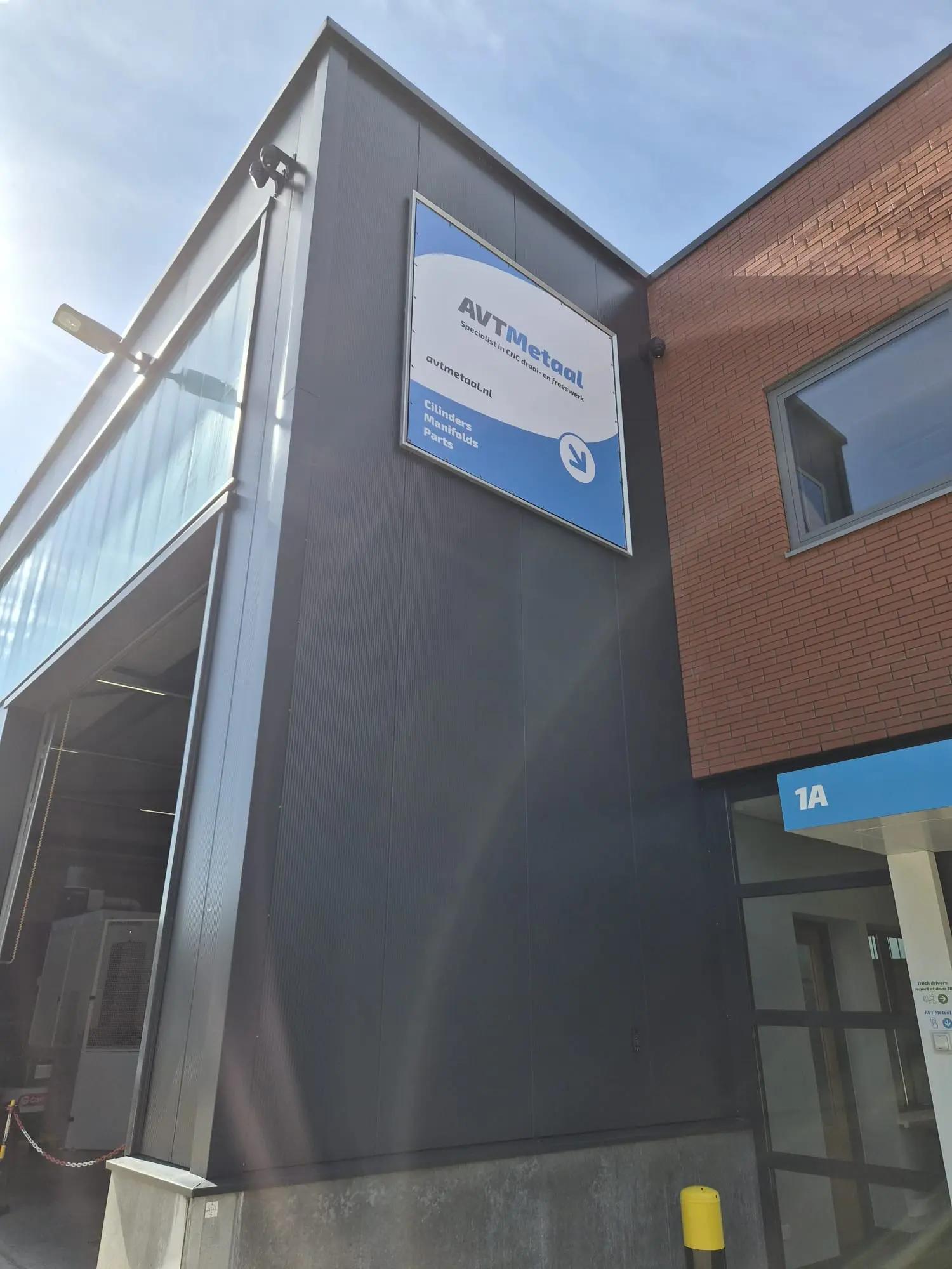 Blauw-wit AVT Metaal reclamedoek in een Triaflex gevelraam, met een pijl richting de ingang.