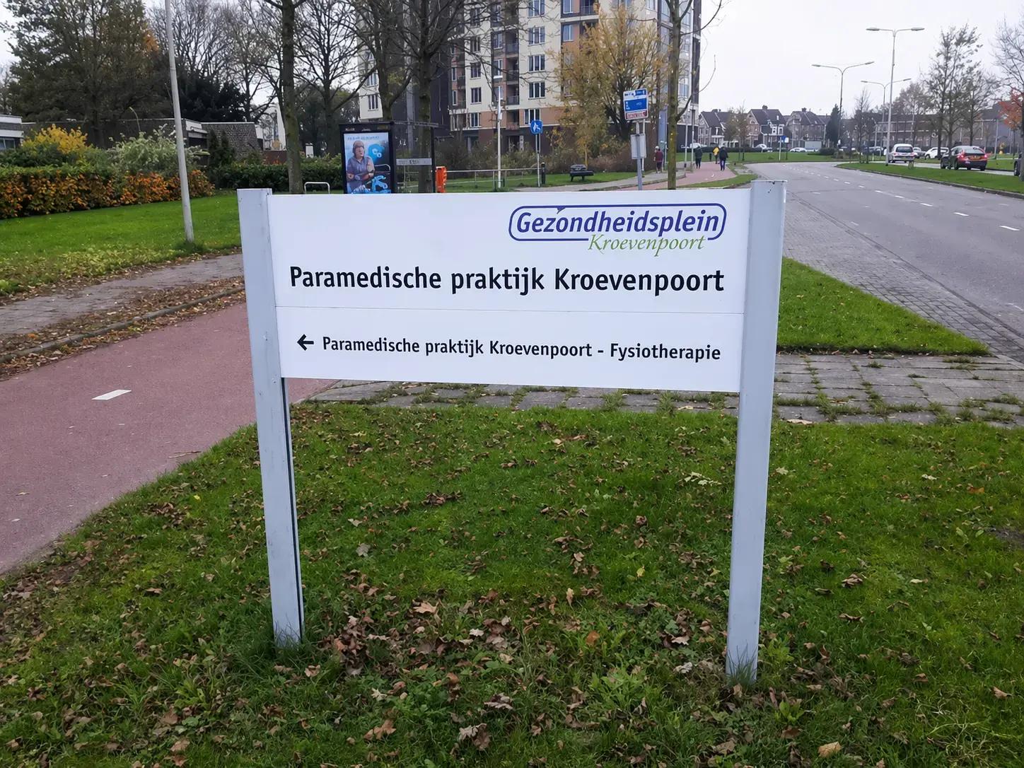 Vrijstaand wit wayfinding-bord van Gezondheidsplein Kroevenpoort met verwijzing naar Paramedische praktijk Kroevenpoort en fysiotherapie, geplaatst langs een grasstrook naast de weg.