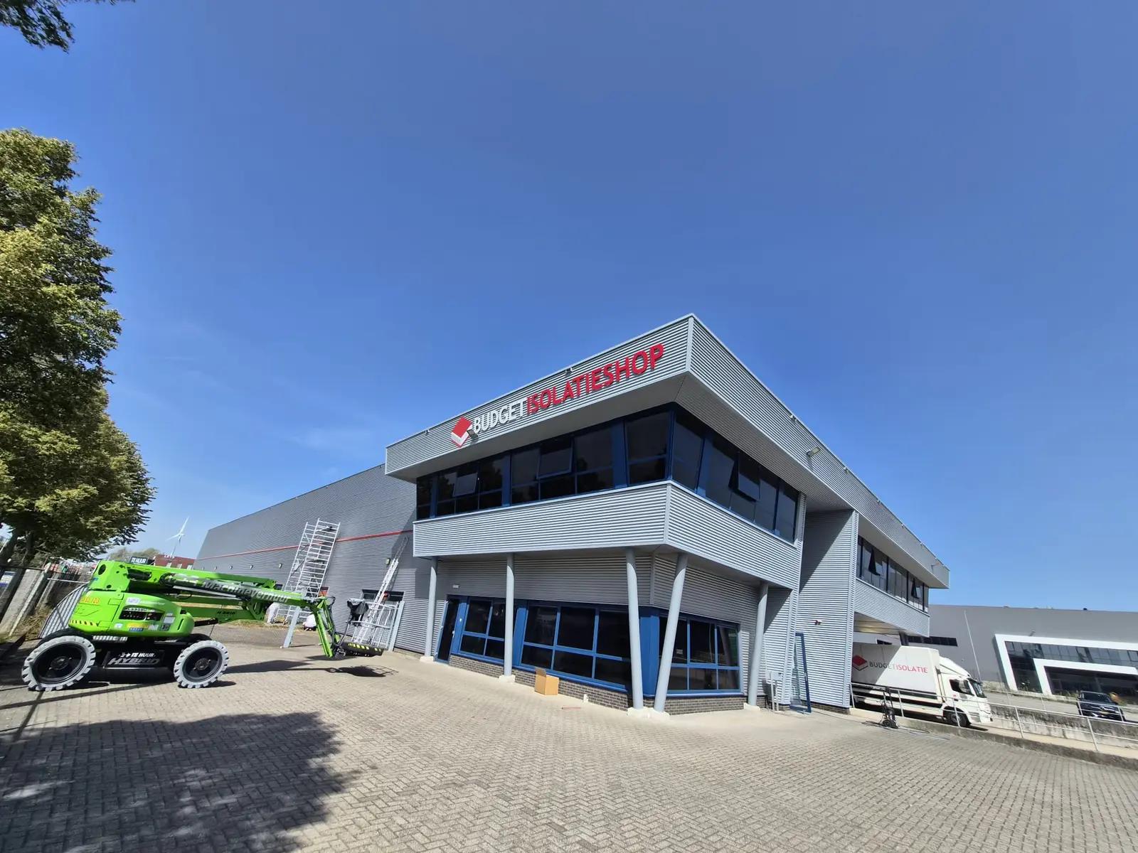 Nieuwe locatie van Budget Isolatieshop met rode en witte gevelletters en een hoogwerker bij het pand.