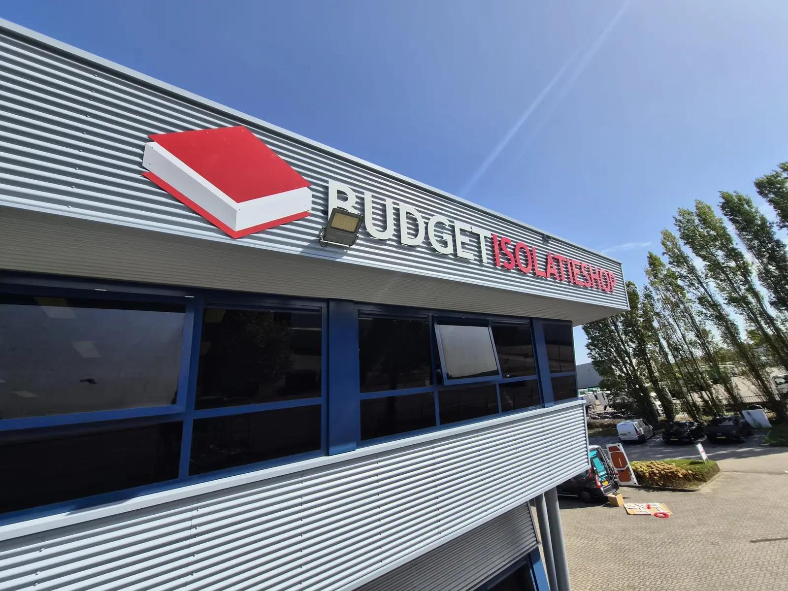 Logo en losse gevelletters van Budget Isolatieshop boven de blauwe raamkozijnen, van dichtbij gezien.