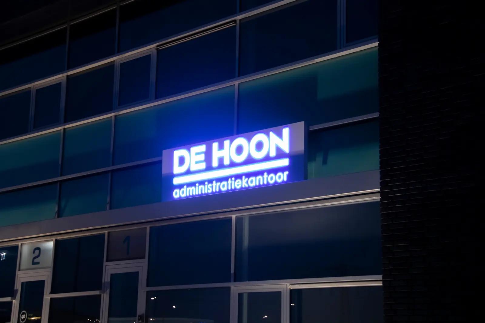 Verlichte naam De Hoon boven de entree in de avond