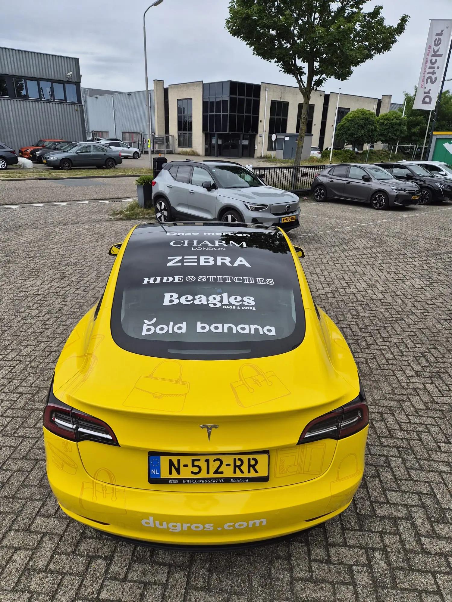 Rear of the yellow Dugros Tesla with bag illustrations, website address and white brand logos on the glass.